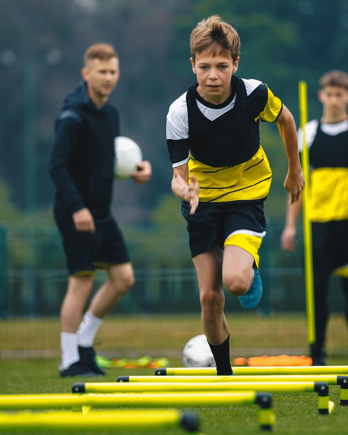 Young footballer sprinting through agility poles at training